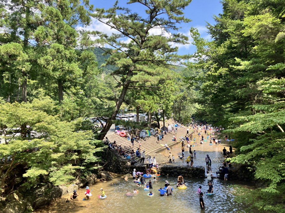 緑の中の川で多くの人が水遊びをしている様子